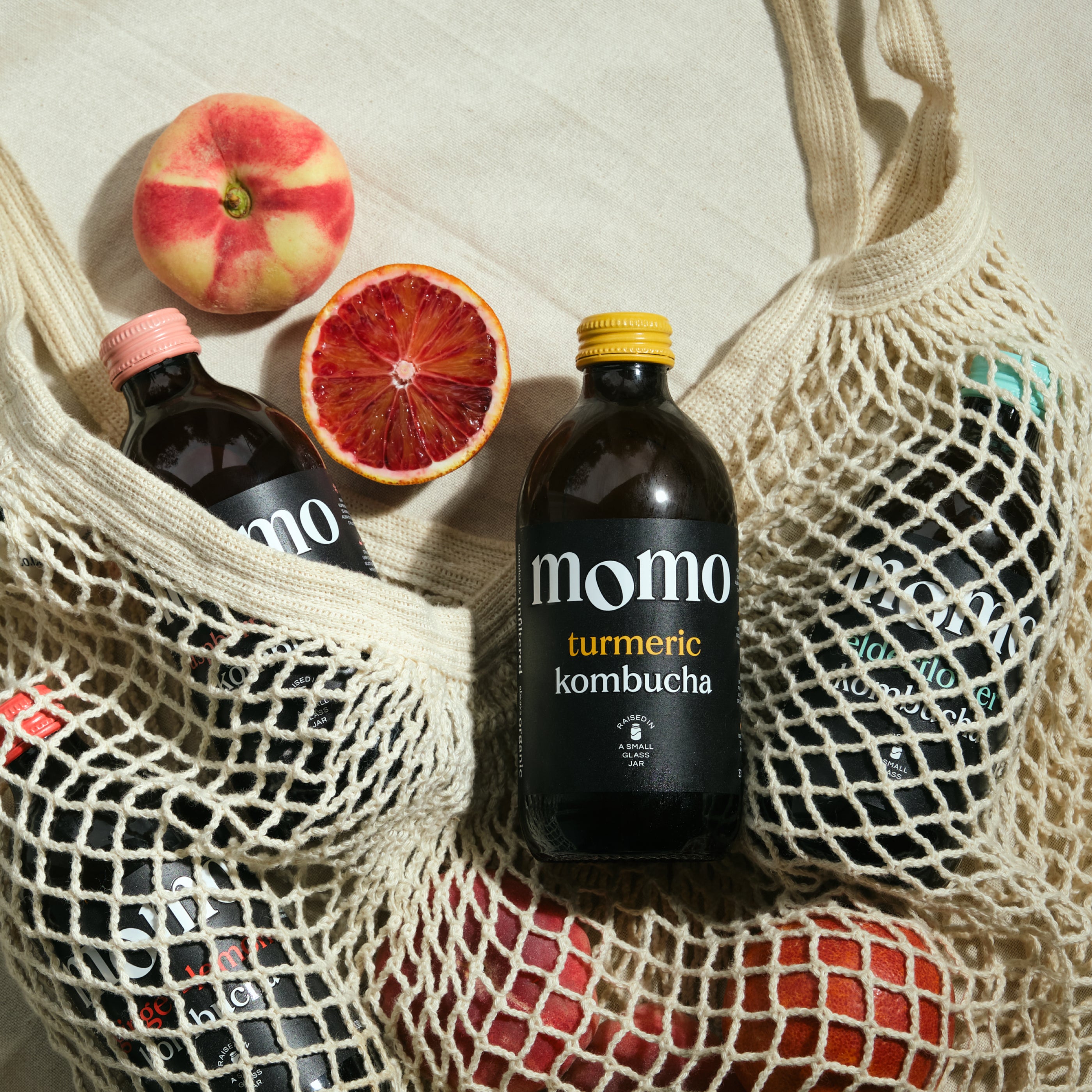 Momo turmeric kombucha bottle with a peach and blood orange on a textured surface